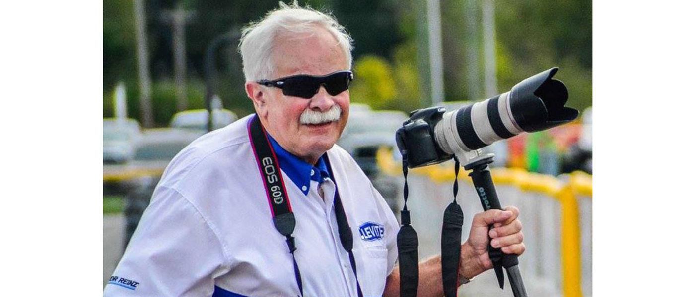 Bill McKnight in MAHLE Clevite logo shirt and professional DSLR camera on the side of the drag strip