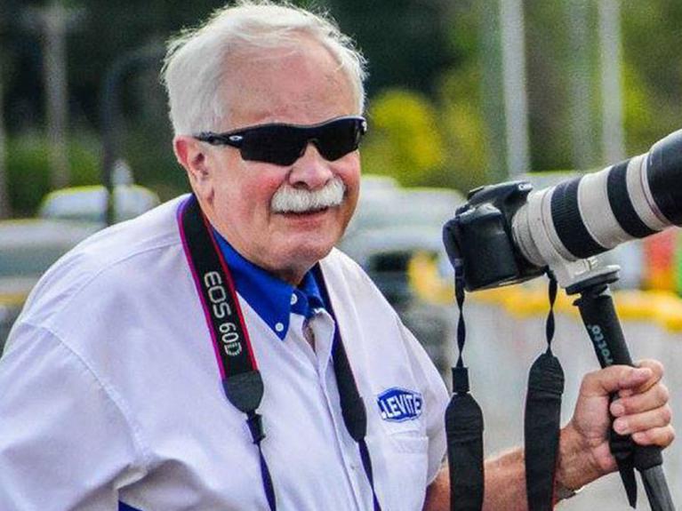 Bill McKnight in MAHLE Clevite logo shirt and professional DSLR camera on the side of the drag strip