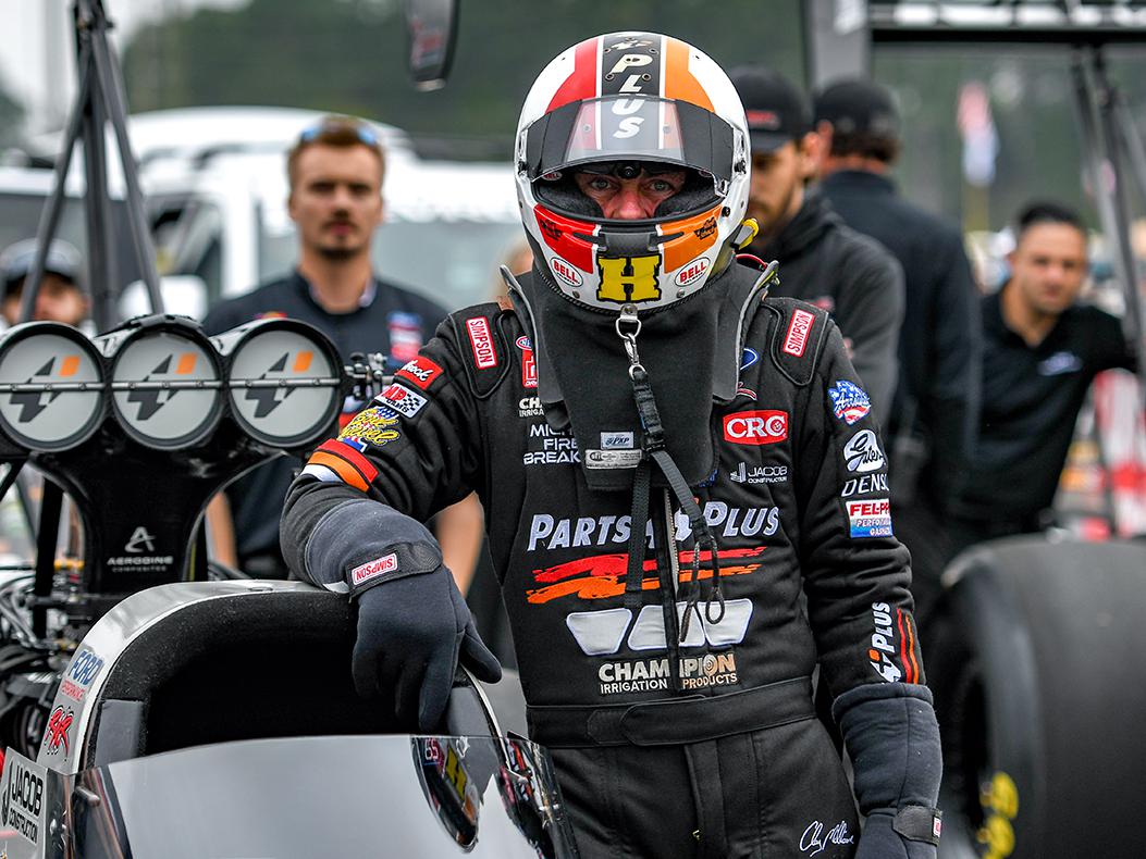 A top fuel drag racer stands outside the cockpit in his firesuit and helmet.