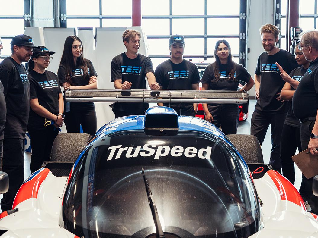 TruSpeed students gathered around a car listening to an instructor. 